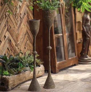 Two decorative holders with a rustic design, one small and one large, made to hold candles or seasonal displays, placed on a wooden surface with a plant in the background.