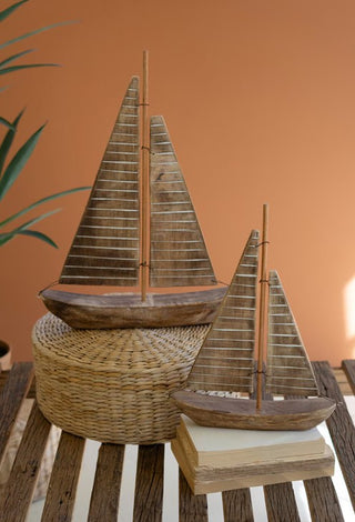 Two rustic recycled wood sailboats, one larger than the other, placed on a wicker surface with a neutral background.
