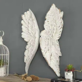 A pair of white ceramic angel wings wall decor placed against a gray background with decorative items around it.