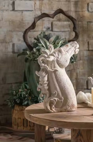 Decorative stone horse figure on a wooden table with a stone wall and plants in the background.
