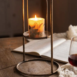 Candle in a metal holder on a wooden table with an open book and a glass of red wine.