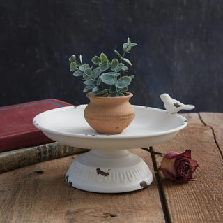 Small white ceramic dish with a plant, bird figurine, and rose on a wooden surface.