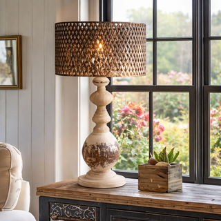 Decorative lamp with wicker shade on a wooden table by a window with garden view