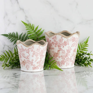 Two decorative ceramic pots with floral patterns on a marble surface with green leaves.